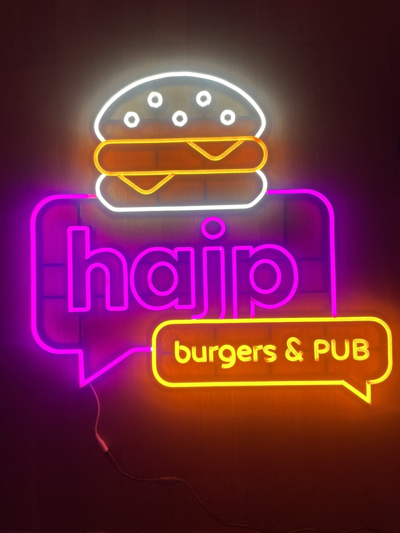 Neon logo lokalu Hajp Burgers & Pub świecący na ceglanej ścianie