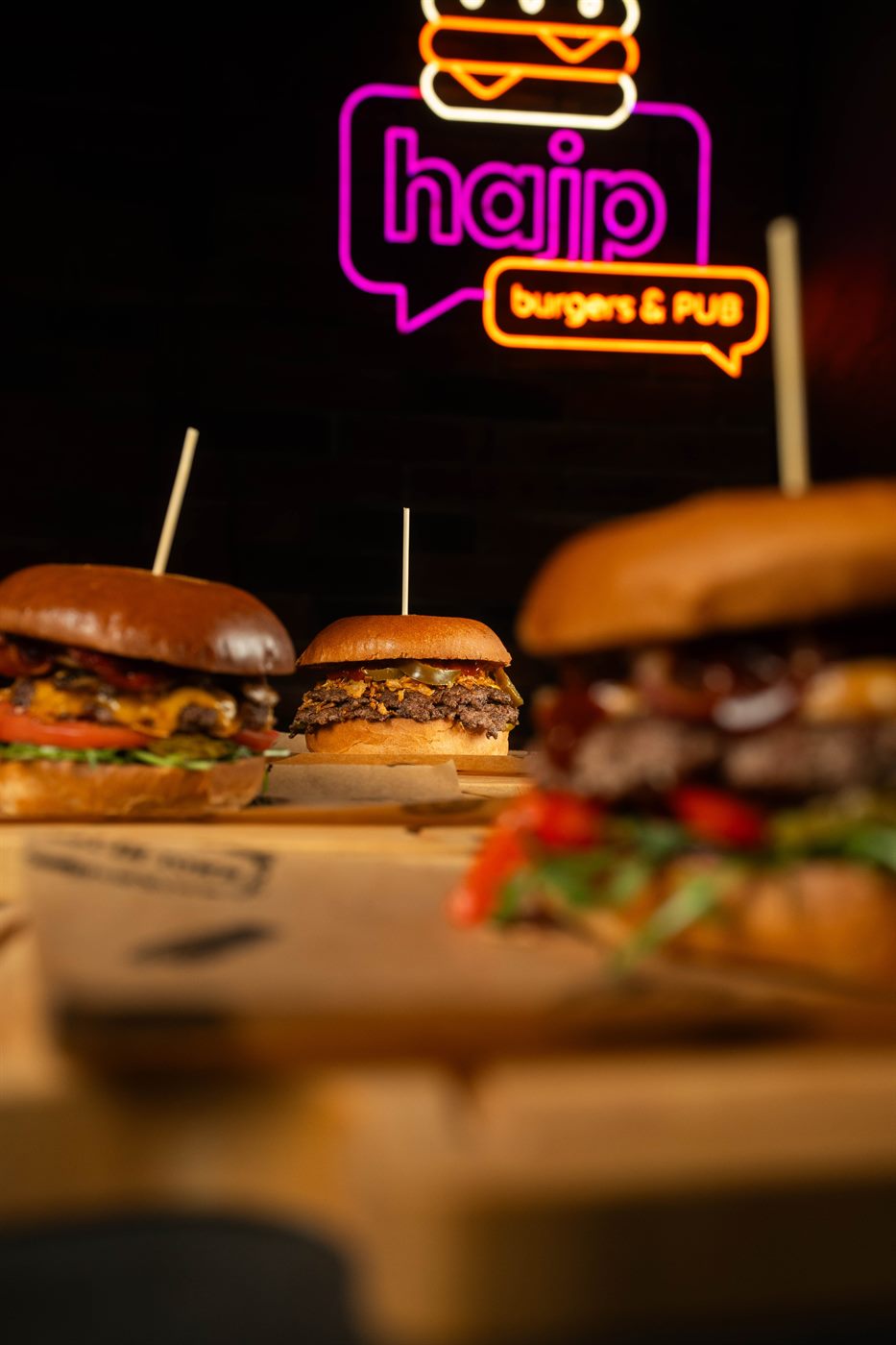 Burgery na desce, w tle świecący neon logo Hajp Burgers and Pub